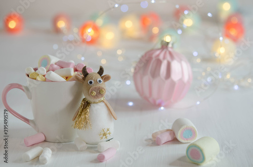 White cup with marshmallows and a toy bull on a blurred background.