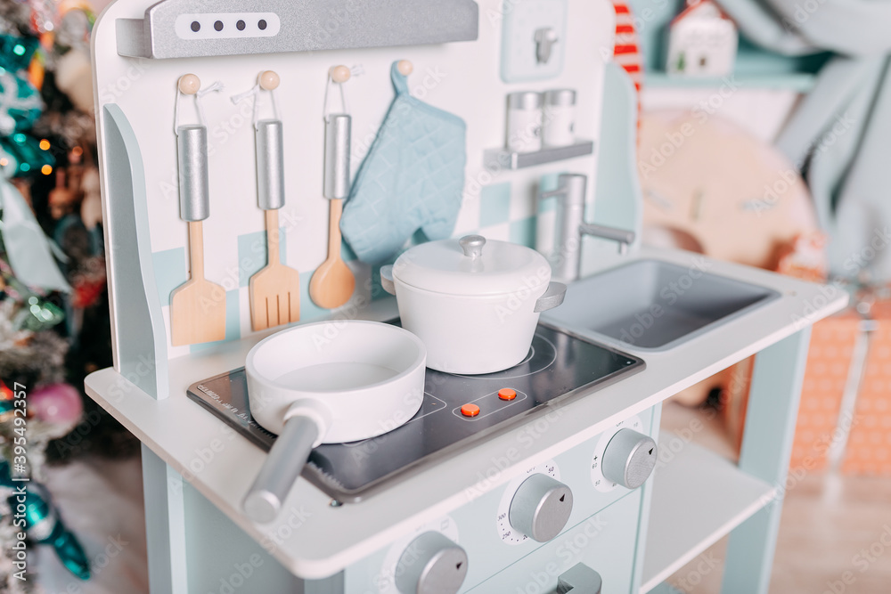 Christmas gifts for kids under the tree. Toy kitchen present for girls. Christmas present under the tree. Toy wooden kitchen and dishes.