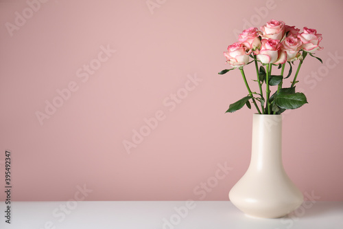 Vase with beautiful roses on white table against pink background. Space for text