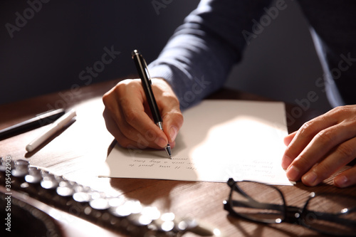 Man writing letter at wooden table indoors, closeup photo