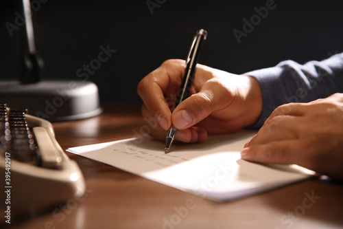 Man writing letter at wooden table indoors, closeup photo