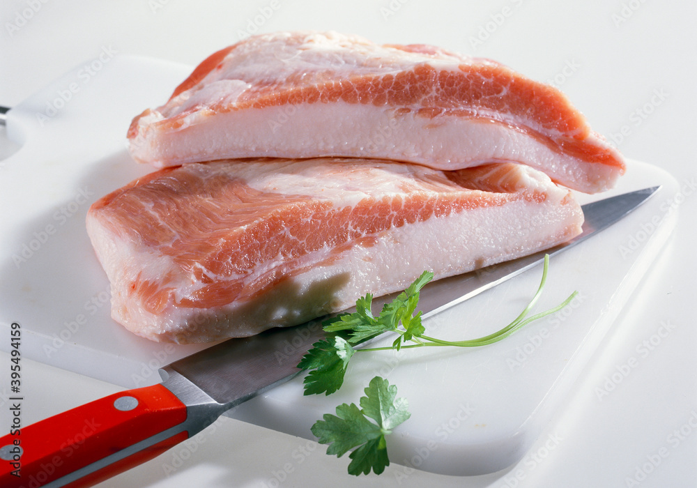 Raw pork cheeks with bacon on a cutting board with a knife Raw pork cheeks with bacon on a cutting board with a knife