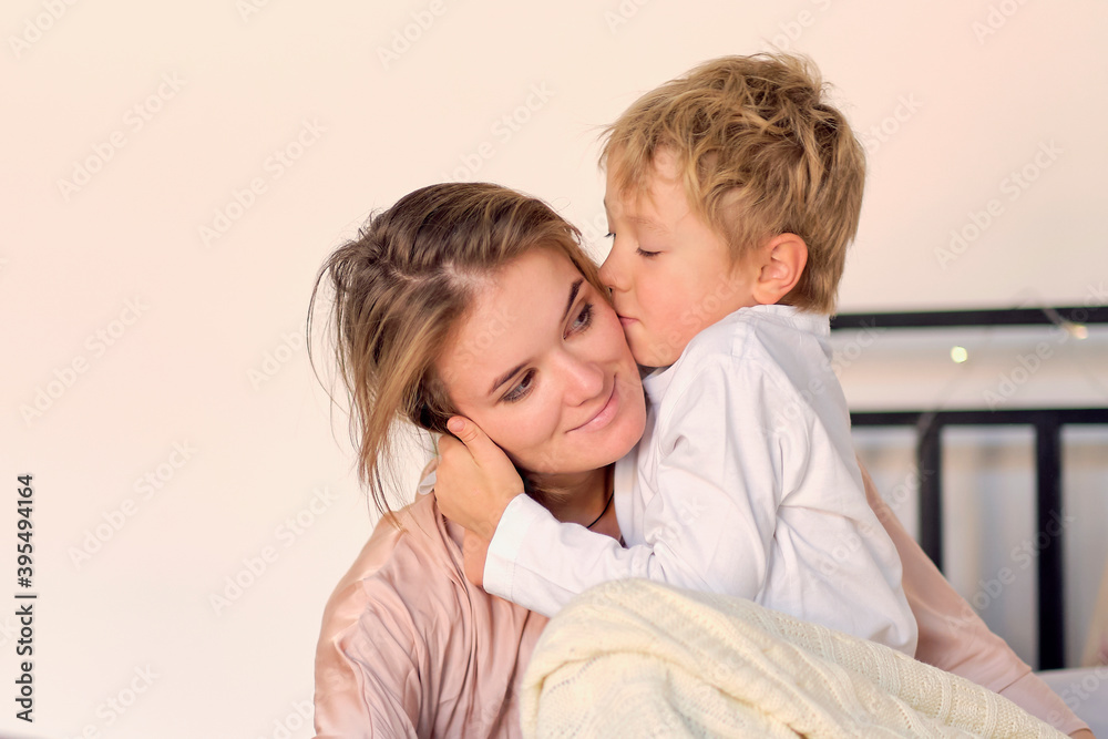 Beautiful woman and her cute little son are hugging and smiling. Boy is kissing his mom in cheek Beautiful woman and her cute little son are hugging and smiling. Boy is kissing his mom in cheek