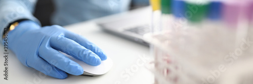 Female hand in rubber glove holds computer mouse in chemical laboratory closeup. Laboratory diagnostics data systematization concept.