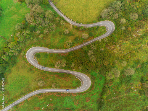 Winding narrow road on a hill in Burren, Ireland. Aerial drone view. Green fields and small trees around the pass.