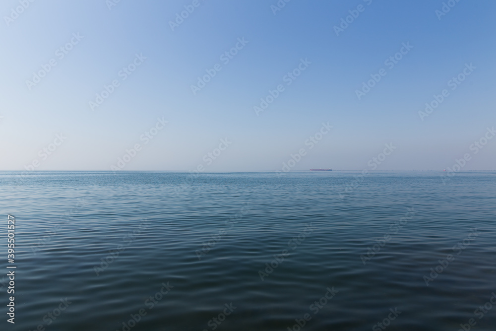 seascape of aegean sea with a faint hazy tanker ship boat in the horizon. blue sky no clouds with blue sea with some small ripple waves