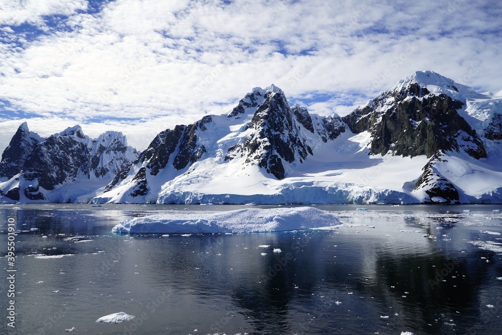 Summer landscape in Antarctica with melting snow, sea, white clouds, icebergs.