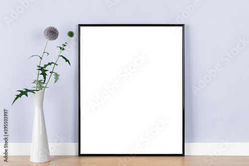 Poster artwork mockup template with black picture frame and globe thistle in vase in front of pastel purple wall, blank image area masked with clipping path