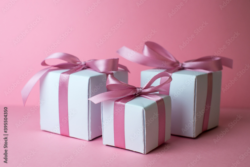 Fototapeta premium Gift or present box with shiny balls, ribbons and snowflakes on pink background. Flat lay composition for christmas, female Christmas. White gift with pink ribbons. A gift box isolated on pink 