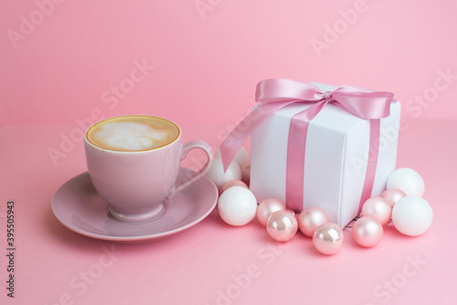 Gift or present box with shiny balls ,coffee, ribbons and snowflakes on pink background. Flat lay composition for christmas, female Christmas. White gift with pink ribbons. A gift box isolated on pink