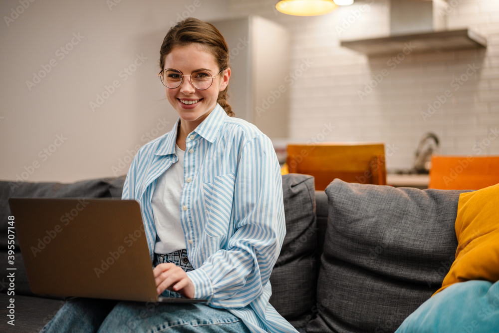 Beautiful smiling girl working with laptop while sitting on couch Beautiful smiling girl working with laptop while sitting on couch