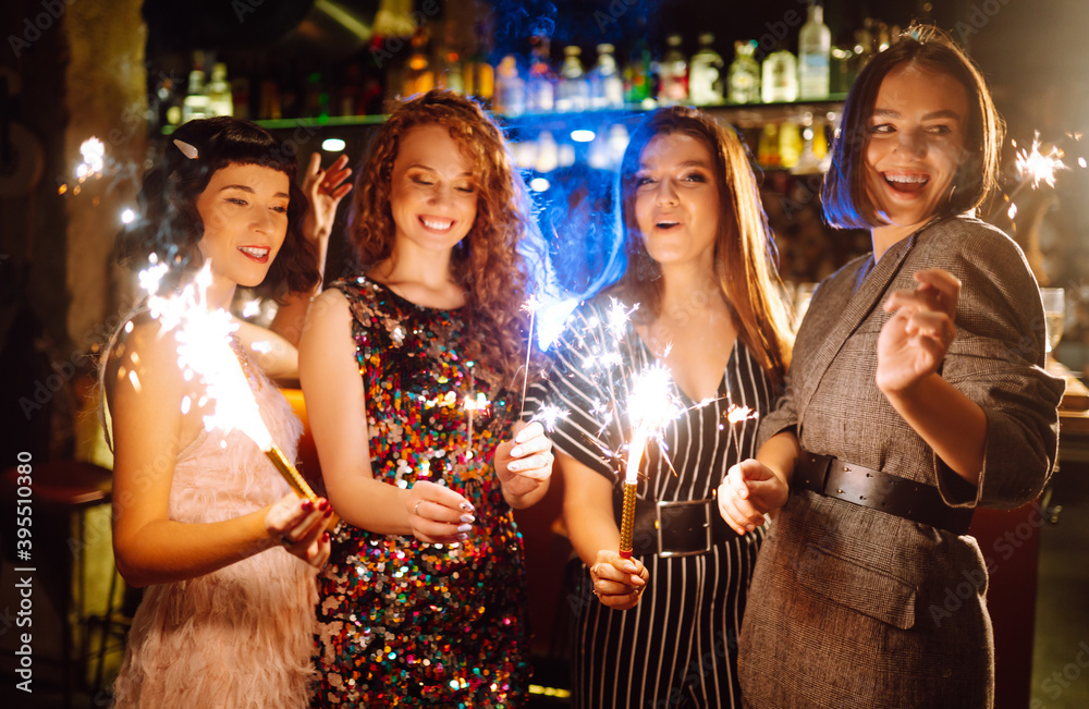 Cheerful women holding sparklers at the party. Four girlfriends clinking glasses of champagne and enjoying new years eve with fireworks. Celebration, bachelorette party, birthday, winter  holidays.