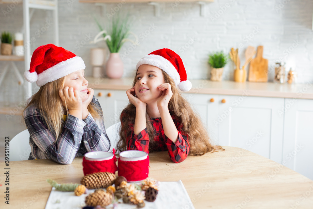 Fototapeta premium Merry Christmas and Happy Holidays! Cheerful cute kid girls having fun. Children in Santa hats have fun at breakfast in the morning. Loving family