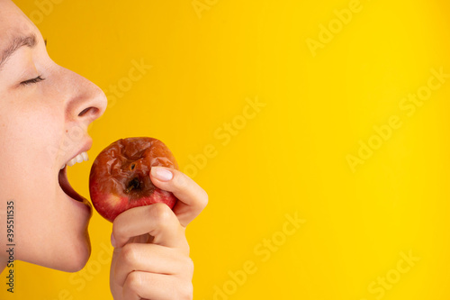 Canvastavla The girl bites a rotten apple with a worm on a yellow background