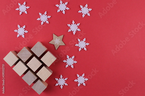 New Year tree made of wooden cubes with white snowflakes on a red background. Red background with wooden christmas tree with white snowflakes