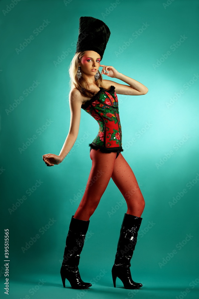 beautiful slender long-legged blonde model in a stylish colorful bodysuit and high hat and fantasy makeup posing in the studio on a birch-colored background beautiful slender long-legged blonde model in a stylish colorful bodysuit and high hat and fantasy makeup posing in the studio on a birch-colored background