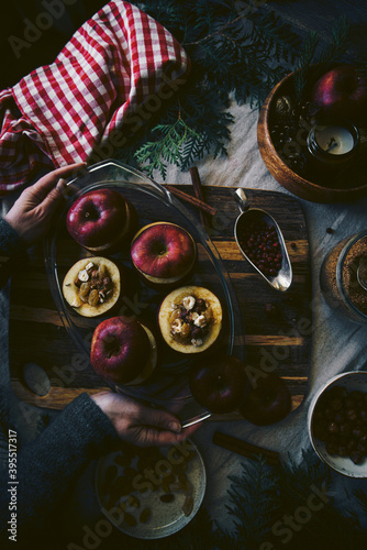 Process of making baked apples. Fresh red apples stuffed with hazelnuts, raisins, lingonberry and brown sugar on wooden board on Christmas table.