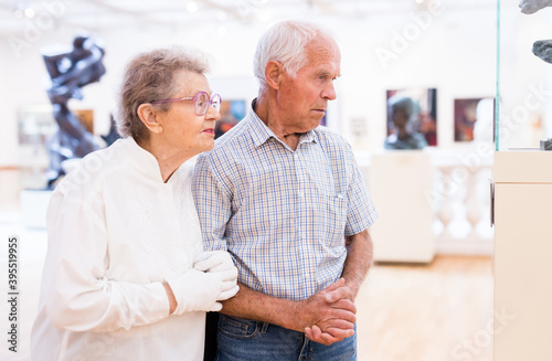 mature European couple examines paintings in an exhibition in hall of art museum