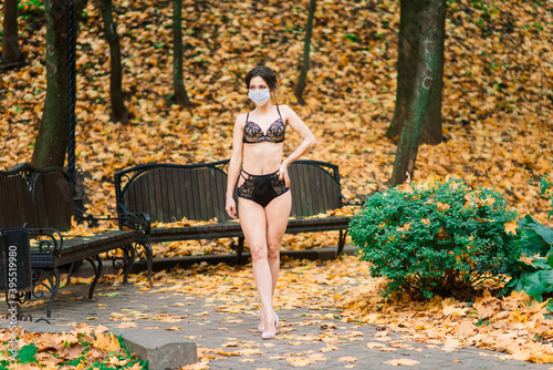 Fashion portrait of sexy woman in mask and lingerie in autumn park. Pandemic, virus, coronavirus