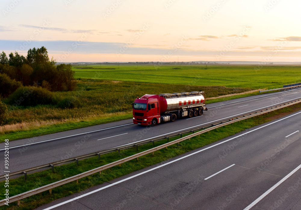 Tank transport of liquid, foodstuff. Metal chrome cistern tanker for food transportation on highway on sunset background.
