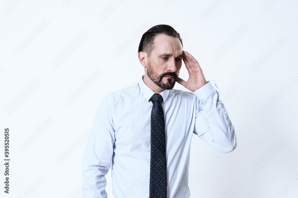 A man touches a sore head while standing on white.
