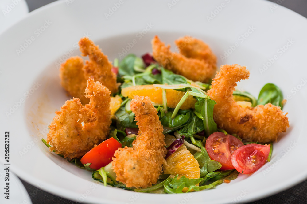 Salad with shrimp in crispy breadcrumbs, citrus mix, cherry tomatoes, fresh cucumber and orange-mustard sauce. Fresh food from restaurant menu