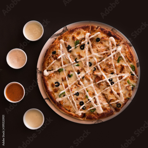 Chicken Tikka pizza with cheese topping with garlic mayo sauce and red chilli sauce on a table