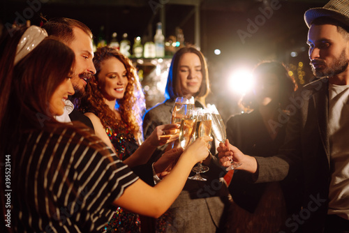 Happy friends clinking glasses of champagne at party in a nightclub. Young people celebrating winter holiday together with champagne. Party, celebration, drink, birthday concept.
