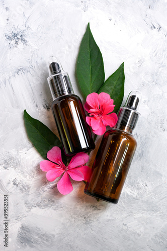 Two dropper bottles for serum cosmetic with flower and green leaves, Beauty product, essential oil, skin care. Flat lay composition on marble background.Copy space for text. Natural care.