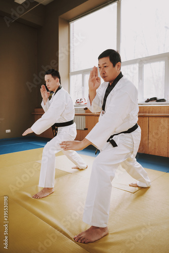 Man in white kimono stands on mats and works out.