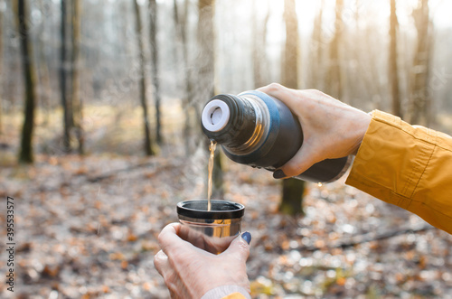 Elderly woman pouring hot tea from a thermos outside. Close-up of senior woman's hand holding a mug with drinks in the forest.