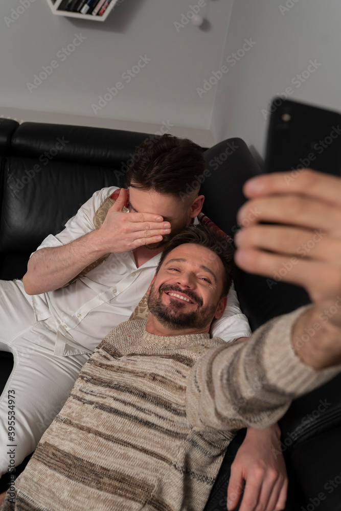 Romantic gay couple using smartphone for video call. One of the boyfriends hiding his face with the hand. Shy partner . High quality photo Romantic gay couple using smartphone for video call. One of the boyfriends hiding his face with the hand. Shy partner . High quality photo