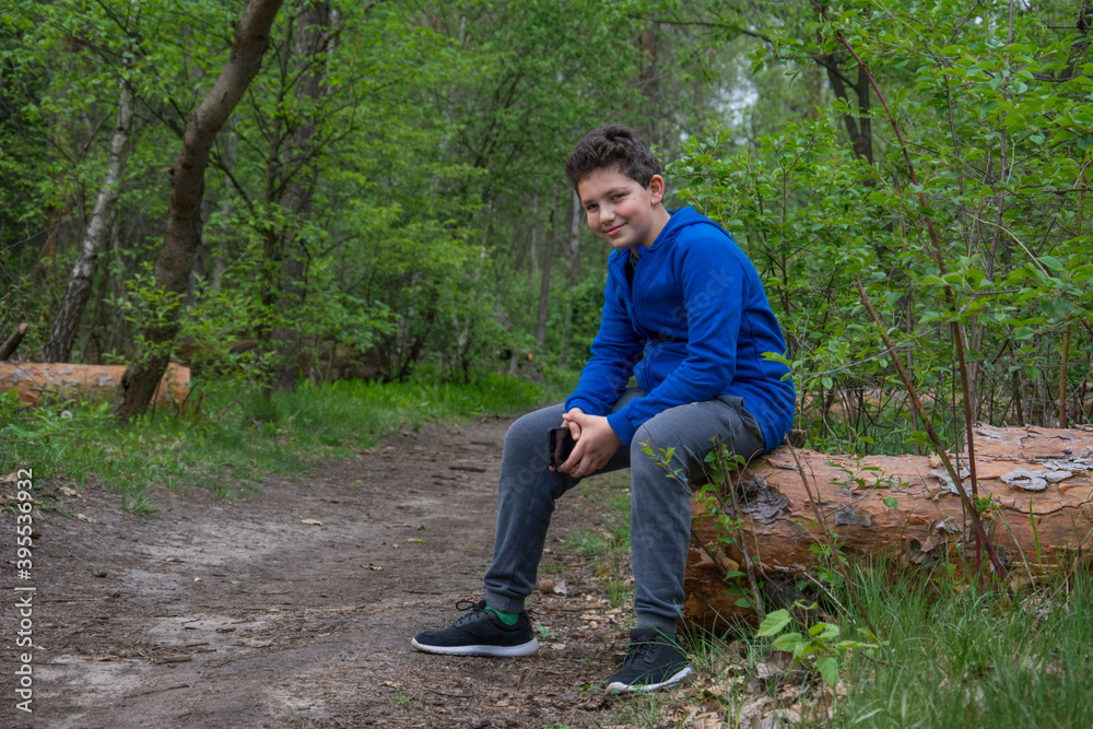 Teen boy sits alone on log in woods and smiles with arms crossed Teen boy sits alone on log in woods and smiles with arms crossed