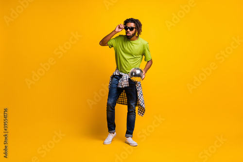 Full size photo of young man hold glitter disco ball enjoy party wear checkered shirt isolated over yellow color background