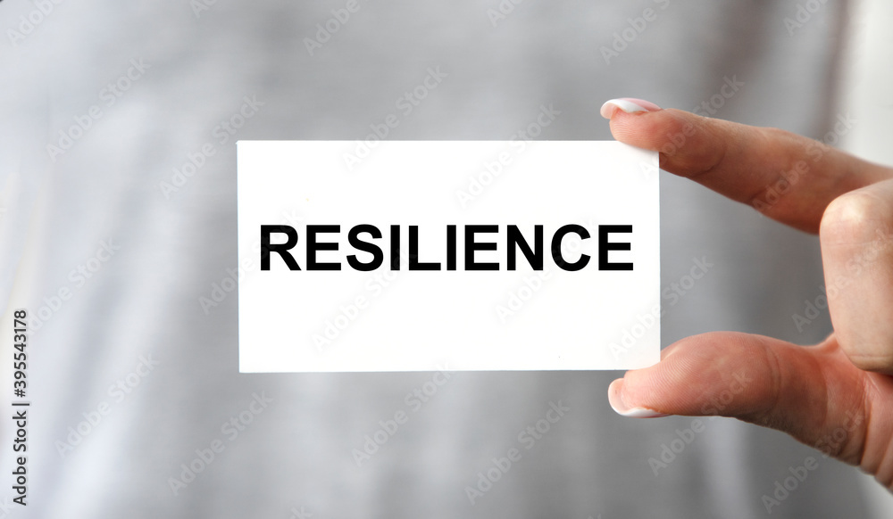 The businessman holds a business card with the text OF RESILIENCE. The businessman holds a business card with the text OF RESILIENCE.