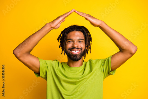 Positive dark skin guy hold hands head new house buyer concept wear green t-shirt isolated yellow color background