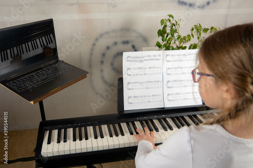 Girl learning to play the piano in distance learning via laptop over the Internet photo