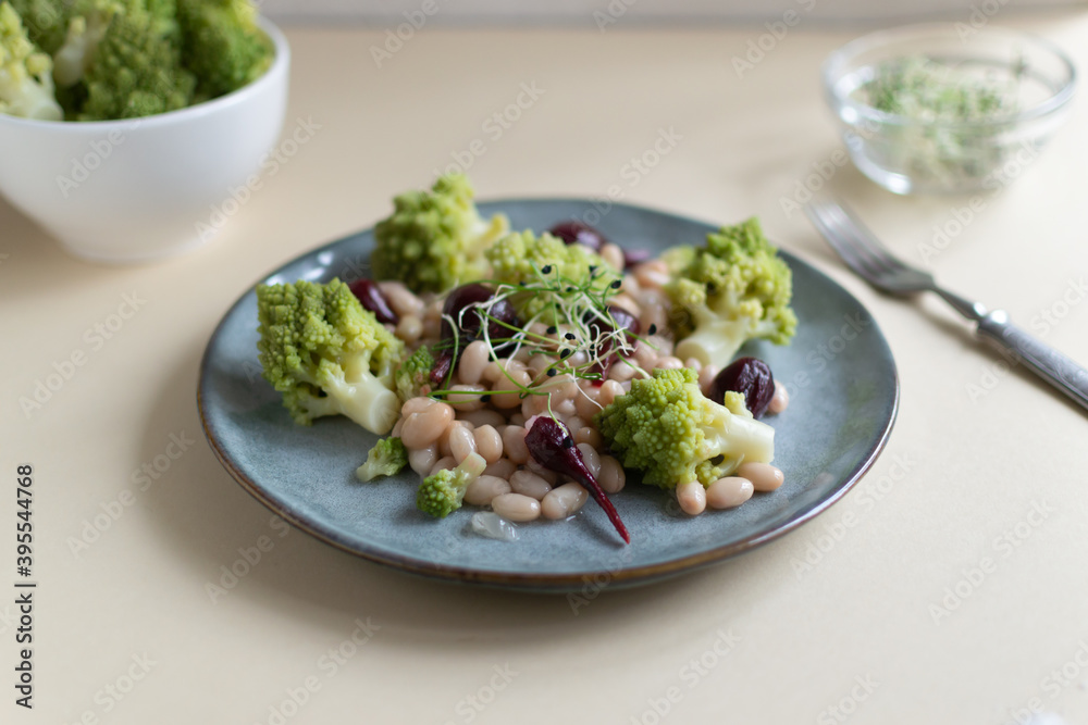 Salad of mini beets, romanesco cabbage, white beans and sprouted onion seeds on a gray plate on a light background. Vagetarian food concept. Selective focus. Salad of mini beets, romanesco cabbage, white beans and sprouted onion seeds on a gray plate on a light background. Vagetarian food concept. Selective focus.