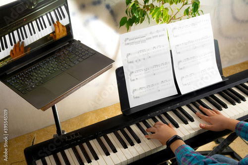 A child learns to play the piano in distance learning via a laptop over the Internet