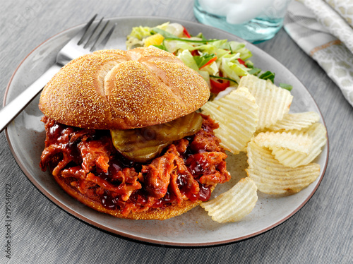 Shredded BBQ Pork with pickles on a Kaiser Roll bun served with potato chips and salad photo