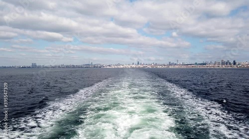 View from a moving boat on the backwash and Istanbul city leaving behind. White clouds on grey sky. Colorful sea with waves. 