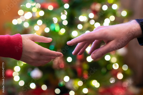 Man and woman two hands reaching for each other on the christmas tree background with glowing bulbs. Close up © flowertiare
