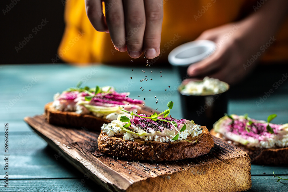 hand sprinkling toast with chia seeds with sliced watermelon radish or chinese daikon, cottage cheese and microgreen. freeze motion. banner, catering menu recipe