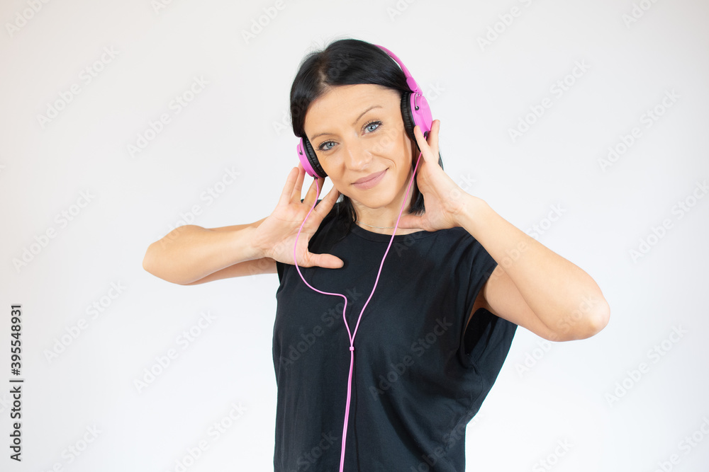 Adorable young woman in black t-shirt having fun while listening to music using earphones isolated over white background Adorable young woman in black t-shirt having fun while listening to music using earphones isolated over white background