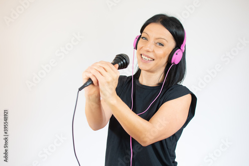 Adorable young woman in black t-shirt singing and having fun while listening to music using earphones isolated over white background