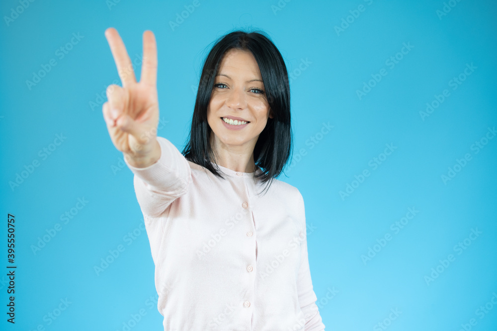 Young brunette woman with blue eyes wearing casual sweater over isolated blue background smiling looking to the camera showing fingers doing victory sign. Number two. Young brunette woman with blue eyes wearing casual sweater over isolated blue background smiling looking to the camera showing fingers doing victory sign. Number two.
