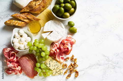 Cheese plate with brie, parmesan, cheddar and meat, fruits and baguette photo