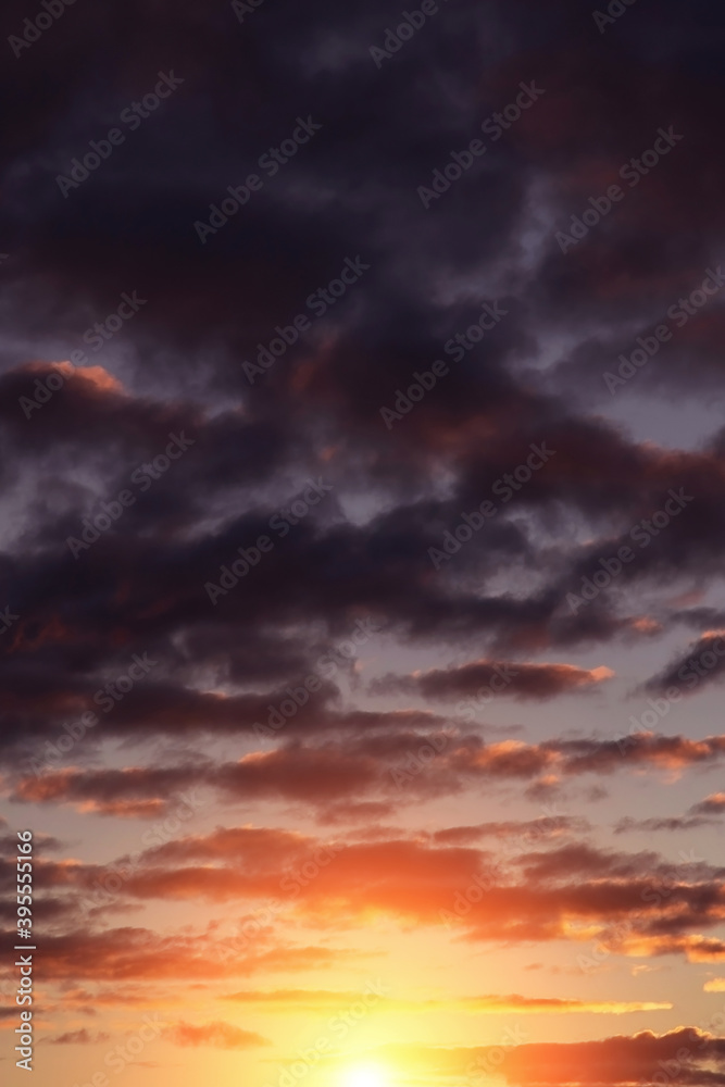 Epic dramatic sunset, sunrise on storm sky with dark blue violet clouds, orange yellow sun and sunlight