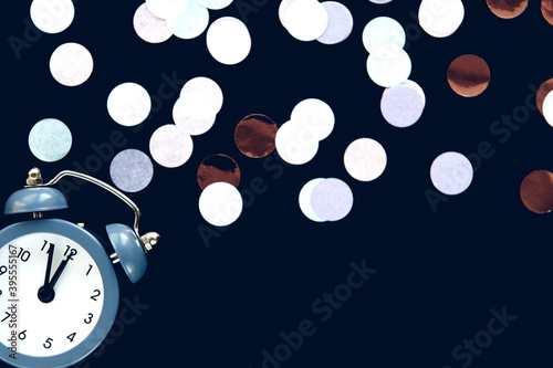 Blue vintage alarm clock shows 12 o'clock isolated on dark background with sparkling round confetti metafan. Wake up and hurry up. Countdown to midnight new year photo