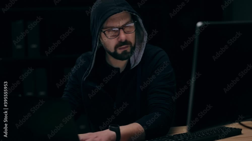 Bearded hacker in glasses copying information from computer to laptop, security information disclosure Bearded hacker in glasses copying information from computer to laptop, security information disclosure